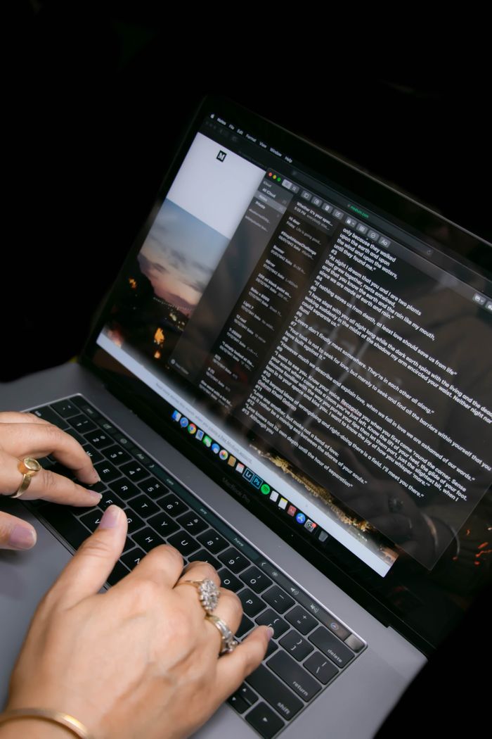 From above of crop anonymous female in golden rings typing on netbook with text on screen on black background in flat